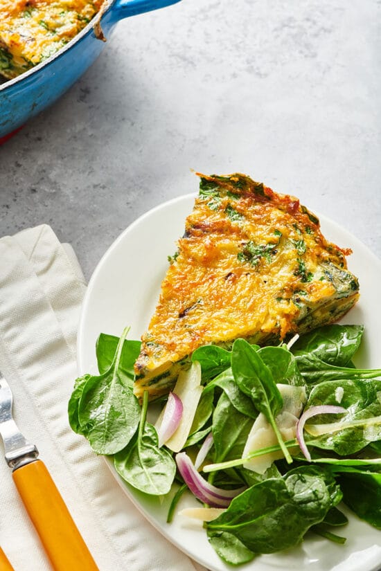 Slice of frittata on plate with leafy greens