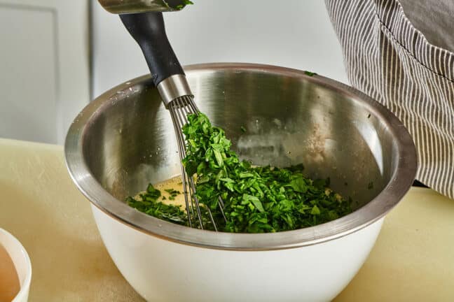 Whisking eggs, spinach, and parsley in stainless steel bowl