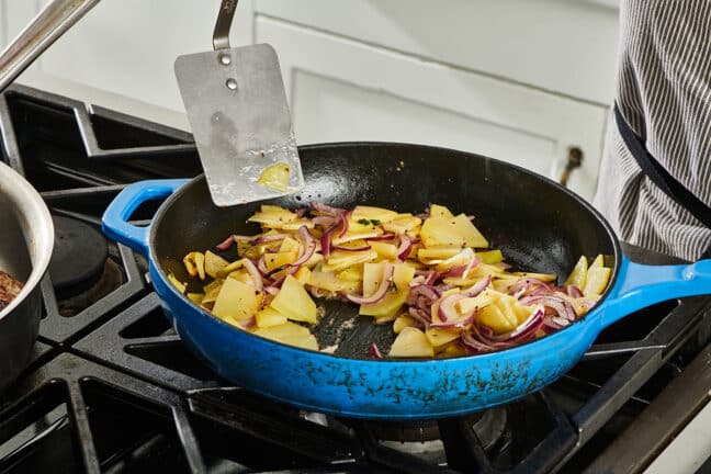 Cooking potatoes and onions in blue skillet on stovetop