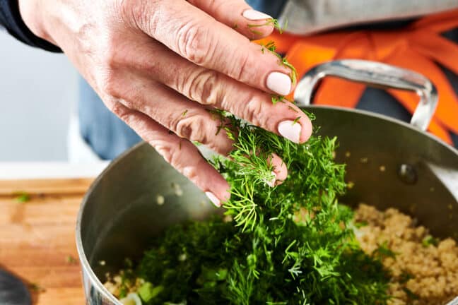 Adding fresh dill to pot of quinoa