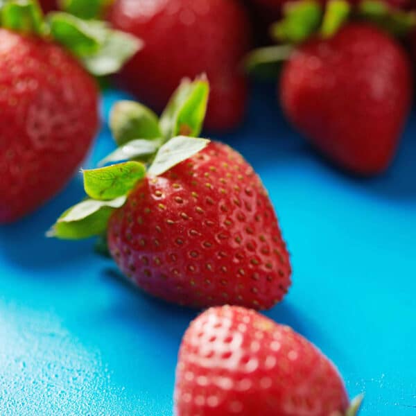 Fresh red strawberries scattered on blue table.
