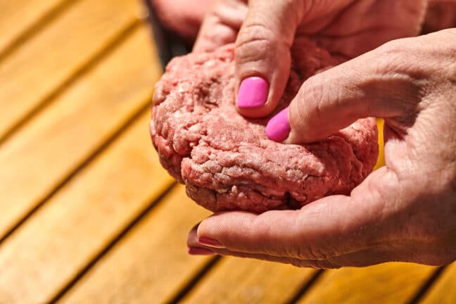 Woman pressing dimple into ground beef burger patty.