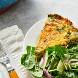 Slice of frittata on plate with salad greens