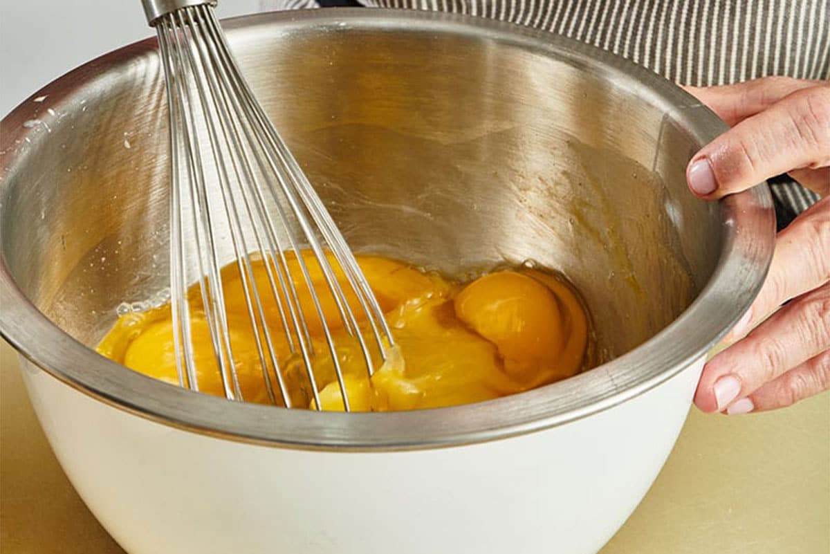 Woman beating eggs with a whisk in metal bowl.