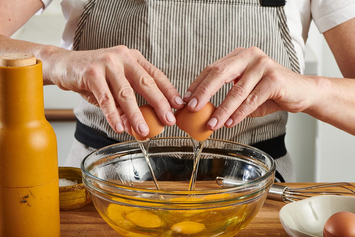 Woman cracking egg into a glass bowl.