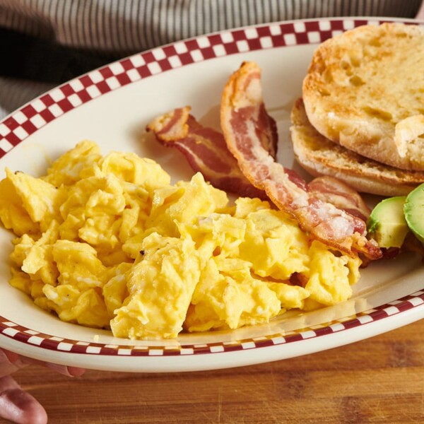 Scrambled eggs with bacon and English muffin on plate.