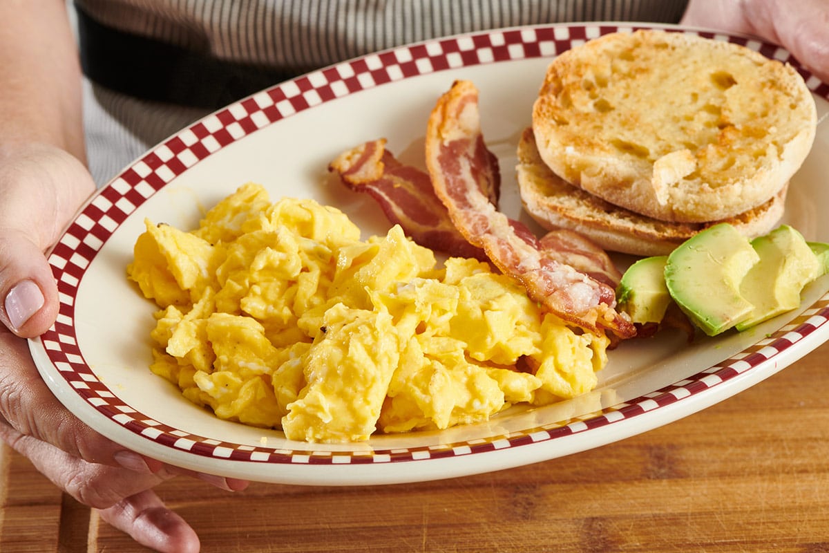 Scrambled eggs with bacon and English muffin on plate.