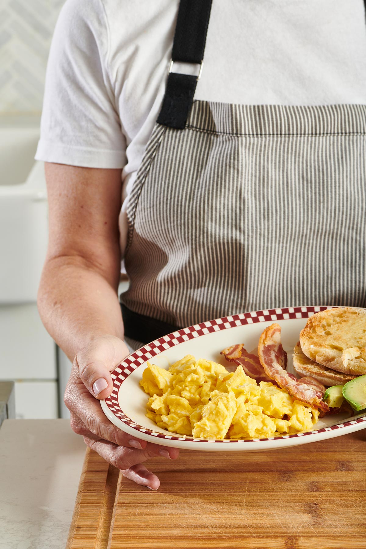 Woman holding plate of scrambled eggs and bacon.