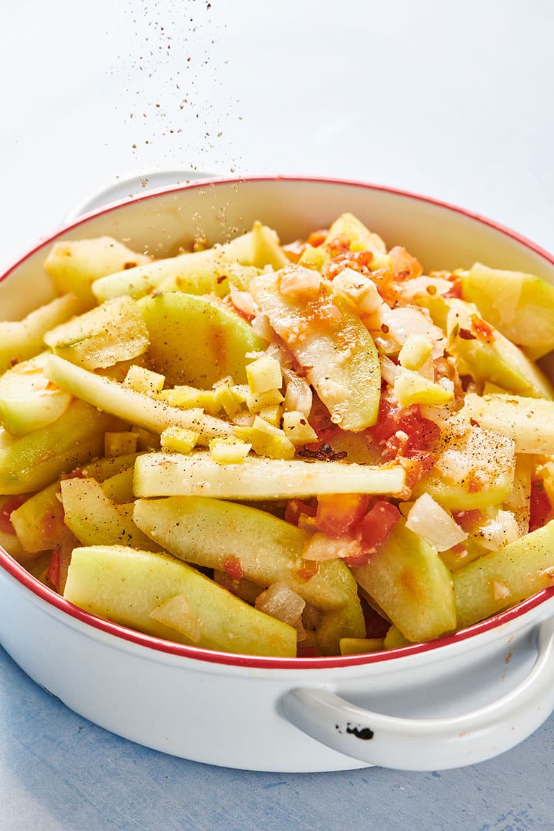 Stewed chayote with onion and tomato in white cooking pot.