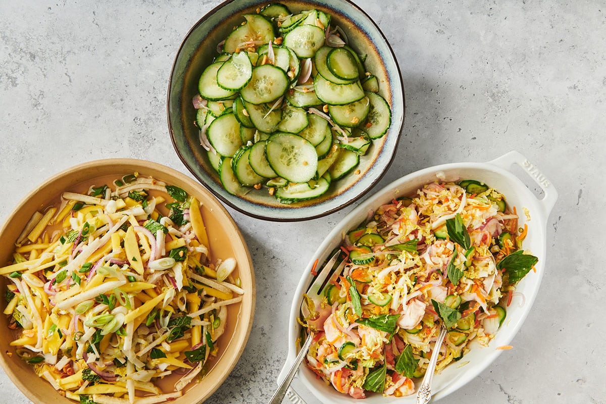 Bowls of Vietnamese dishes with cucumber salad on marble countertop/.