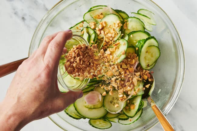 Adding chopped peanuts to bowl of Vietnamese Cucumber Salad