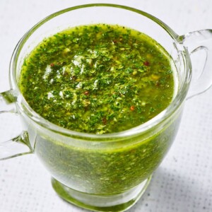 Green Chimichurri Sauce in glass jar on a marble table.