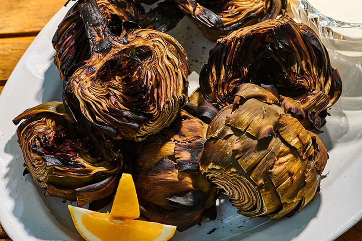 Grilled artichokes, lemon caper sauce, and lemon wedge on plate.