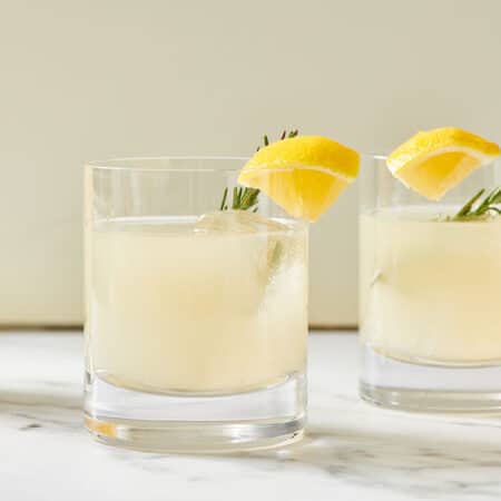 Glasses of Lemongrass Cocktail with rosemary and lemon garnish on marble counter.