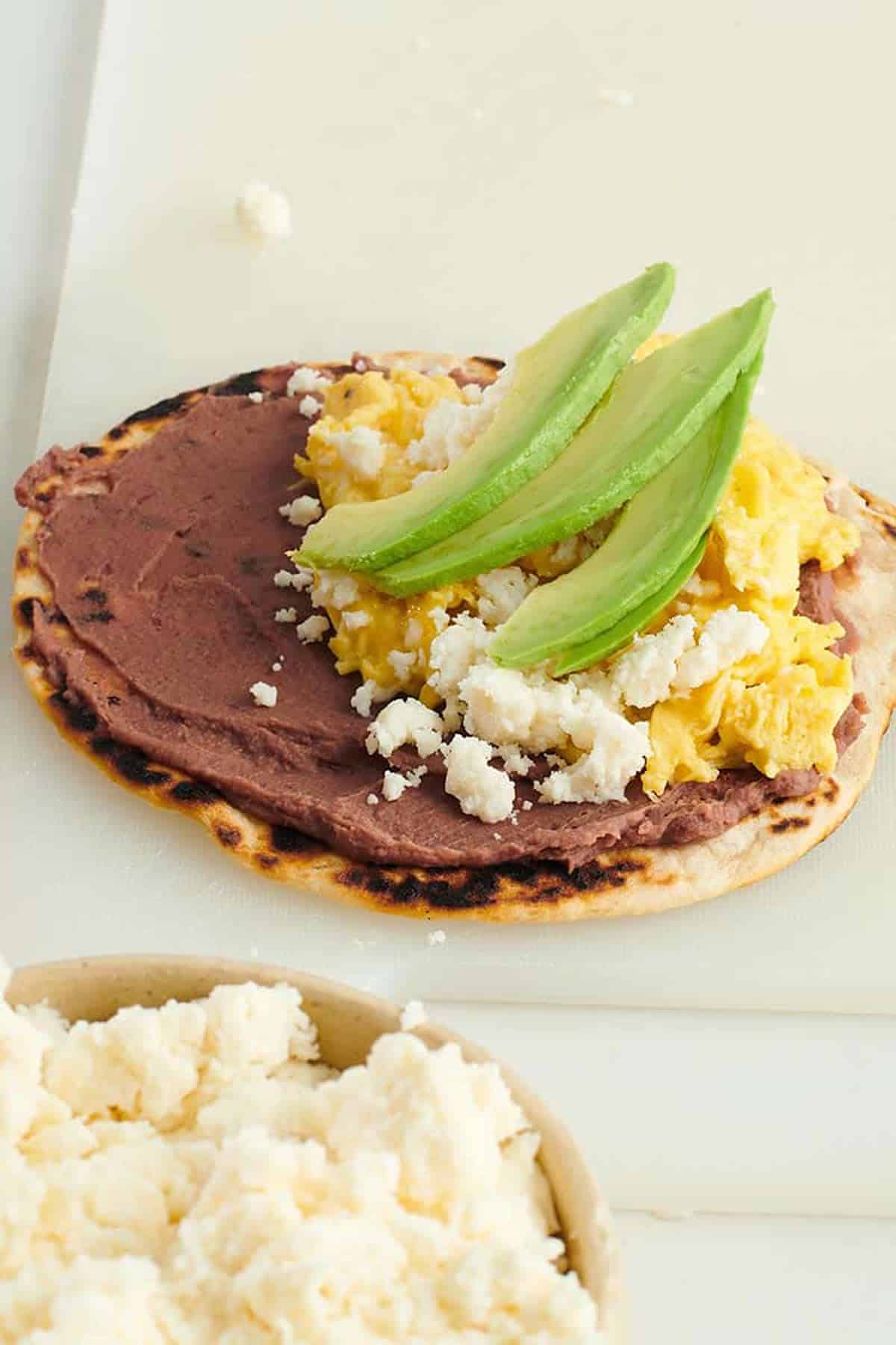 Baleadas with flour tortilla topped with refried beans, queso fresco, and avocado slices.