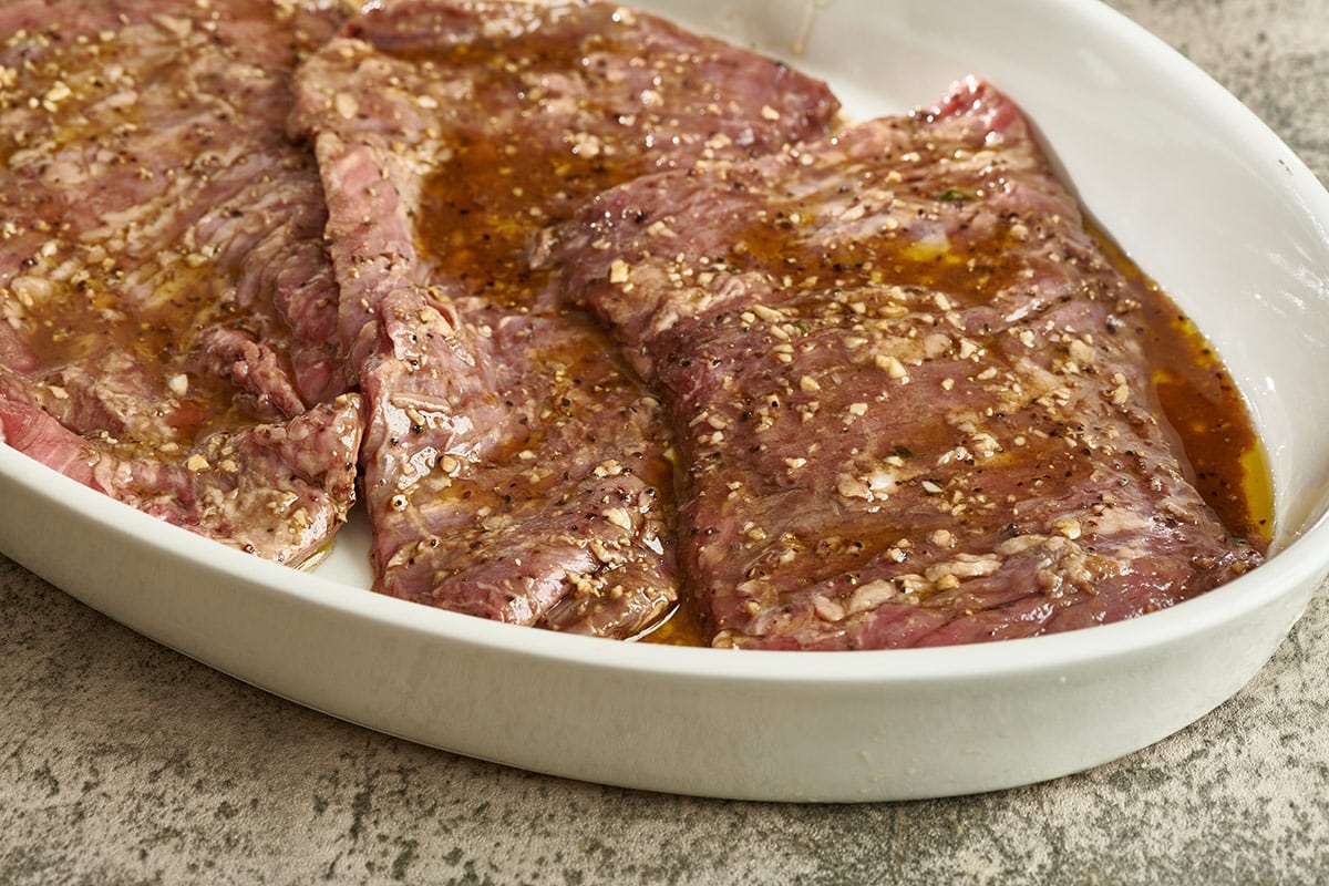 Skirt steaks marinating in a white oven bowl.