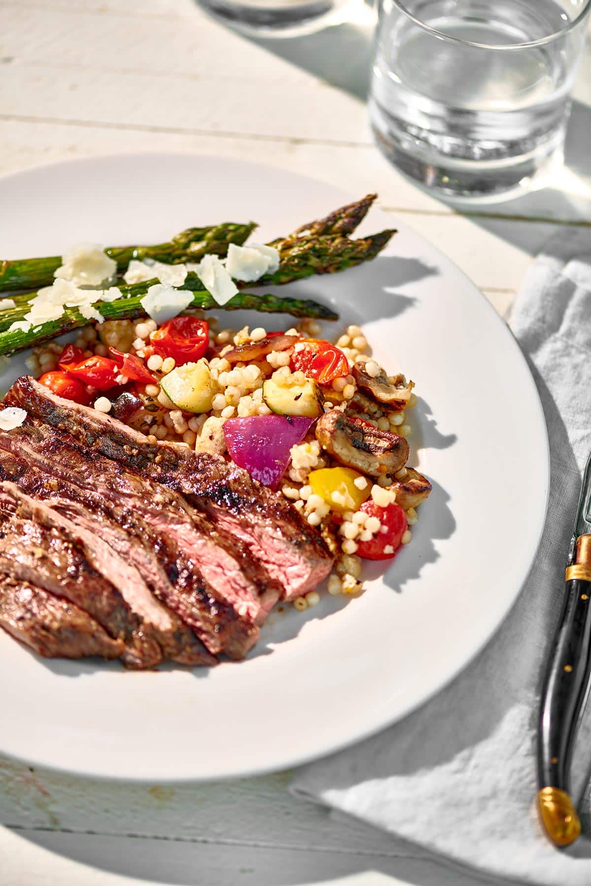 Sliced Balsamic Marinated Skirt Steak on a plate with grilled asparagus and couscous  grilled vegetable salad.