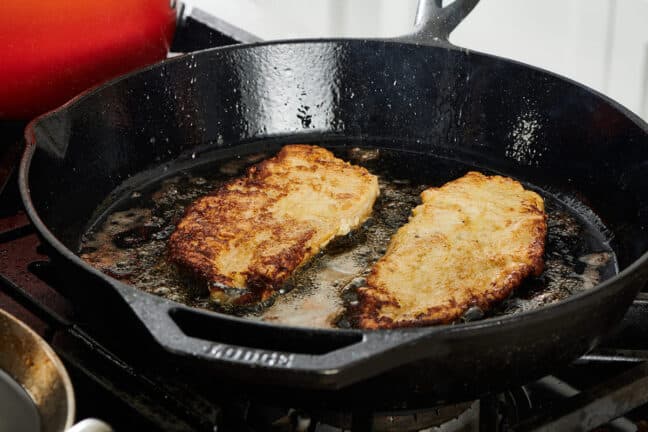 Frying chicken cutlets in cast-iron pan on the stove.