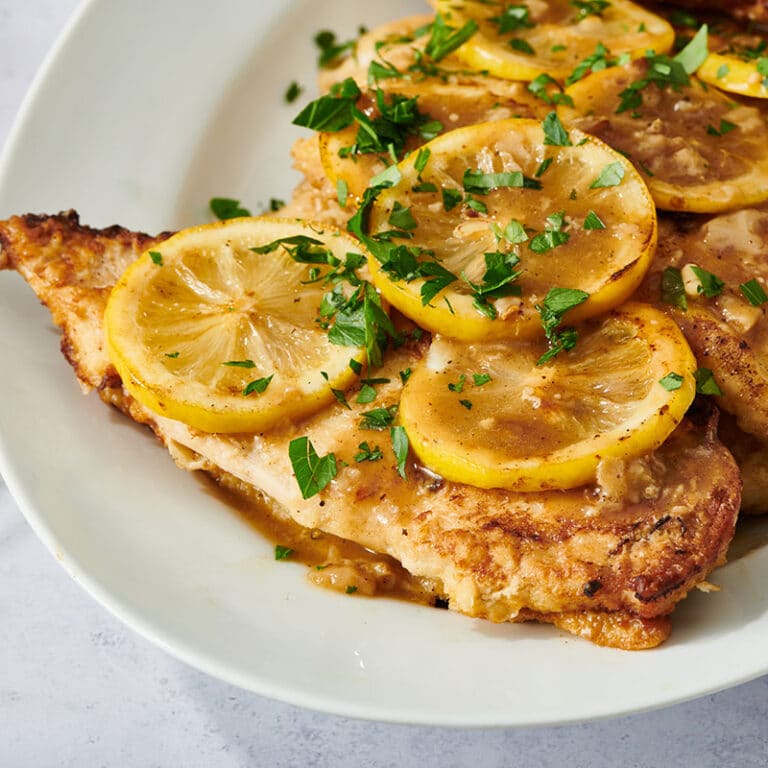 Chicken Francese topped with lemons and parsley on white plate.