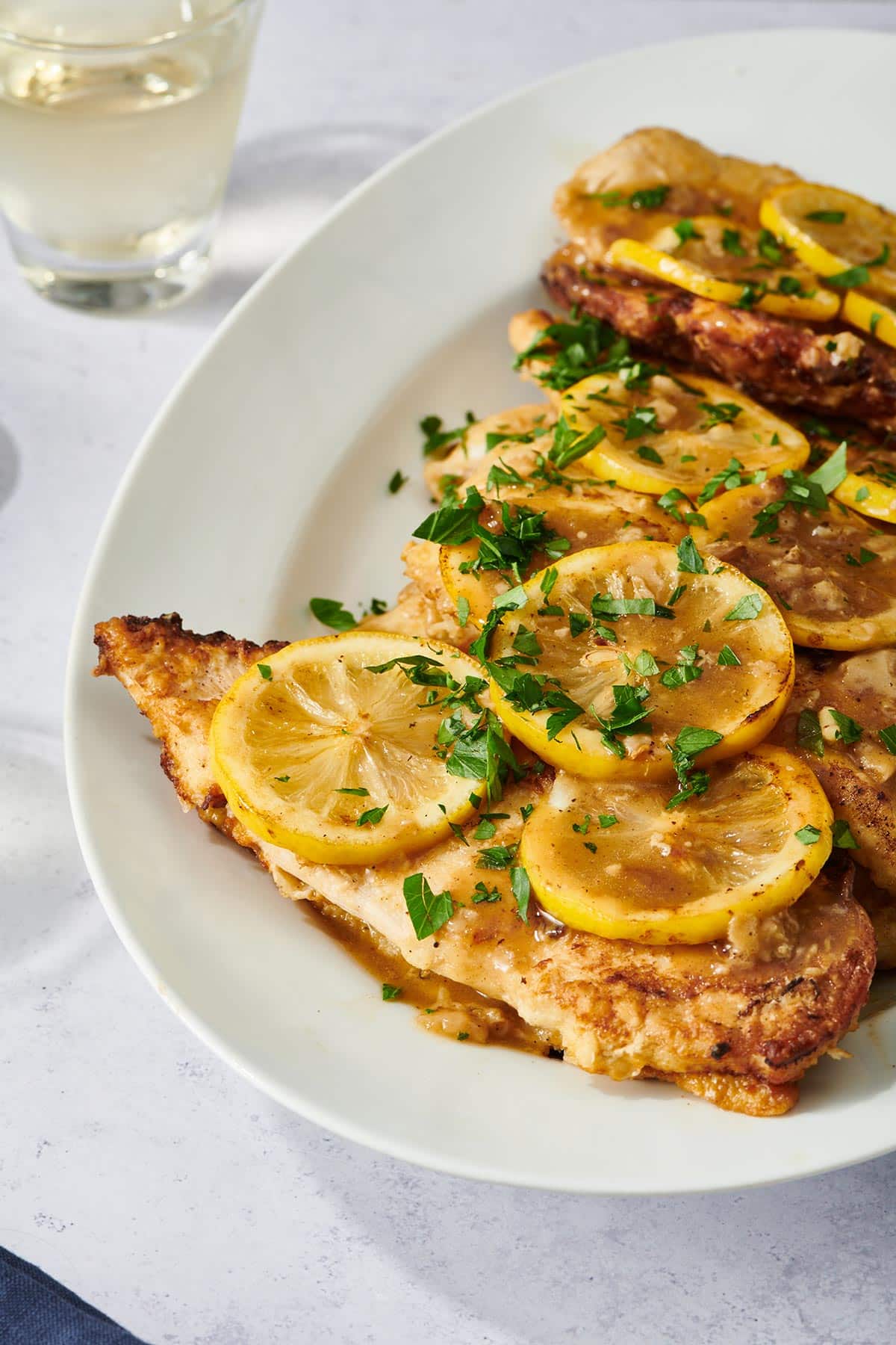Chicken Francese on white plate garnished with lemons and parsley.