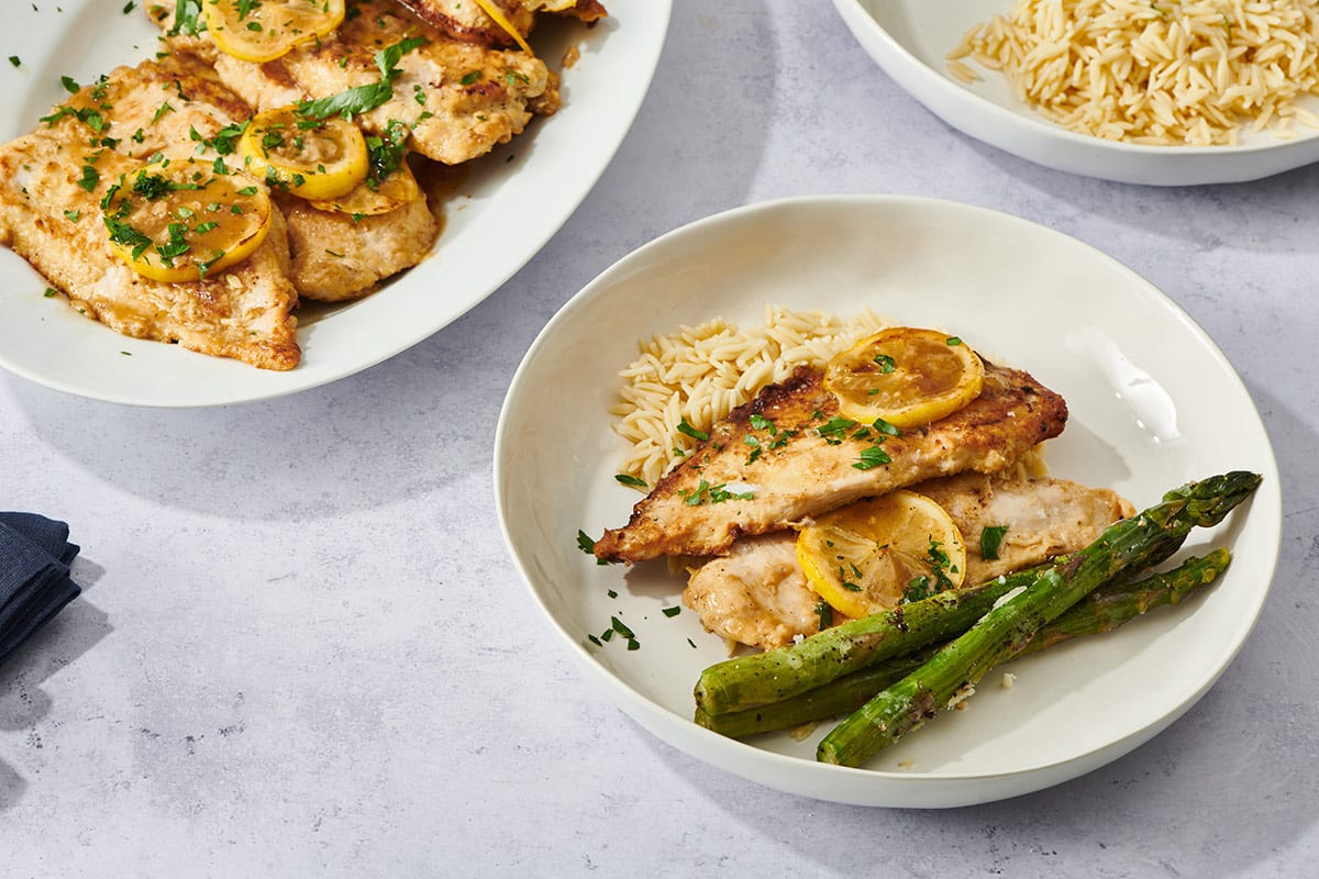 Chicken Francese on a white plate with asparagus and orzo.