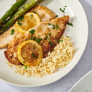 Chicken Francese on a white plate with asparagus and orzo.
