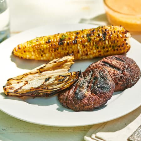 Grilled portobello mushrooms, endive, and corn on the cob on plate.