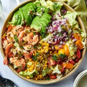 Brown bowl of Grilled Shrimp Salad with avocado on table with white wine.