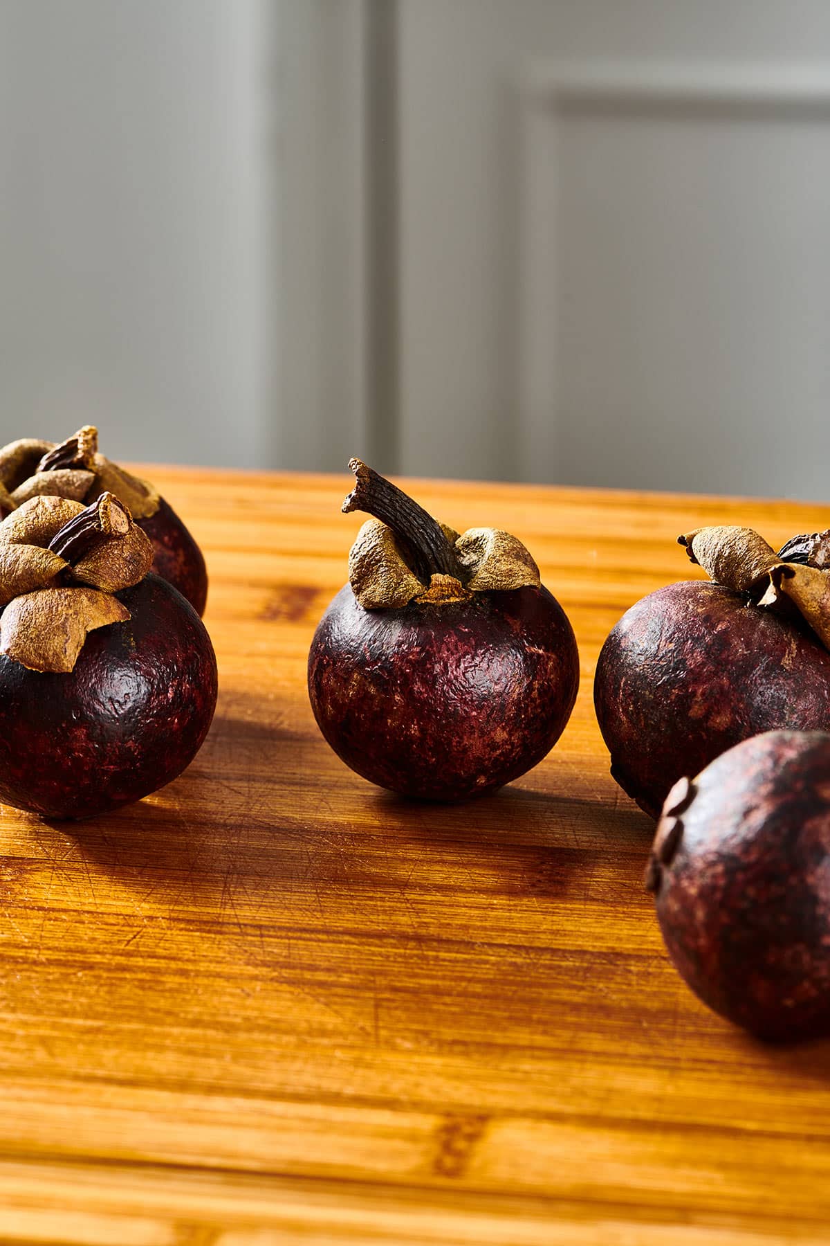 Group of fresh mangosteen fruits on wood cutting board in a kitchen.