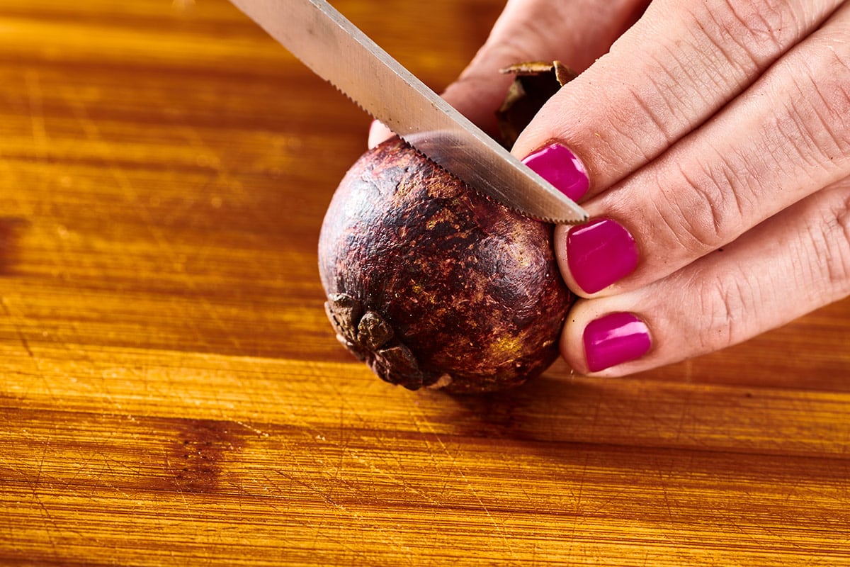 Woman cutting mangosteen fruit open with knife on wood board.