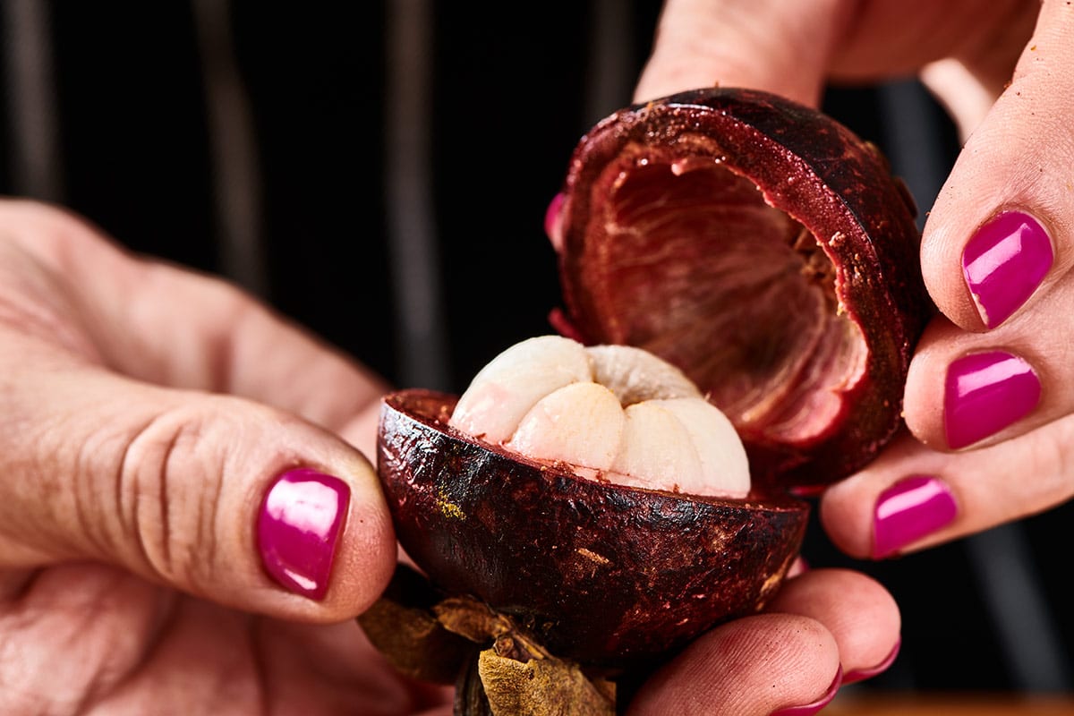 Woman holding an open mangosteen fruit to reveal the white pulp inside.