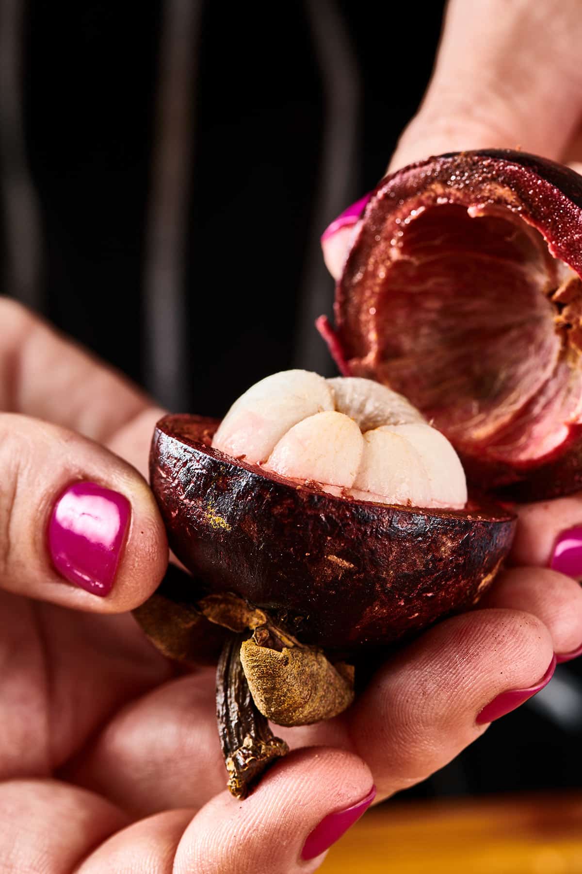 Woman holding an open mangosteen to reveal the fruit's white flesh.
