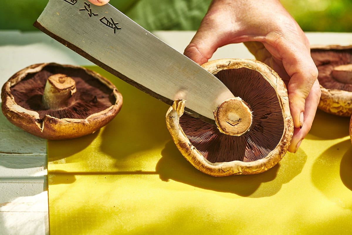 Trimming stems off portobello mushrooms with chef knife.
