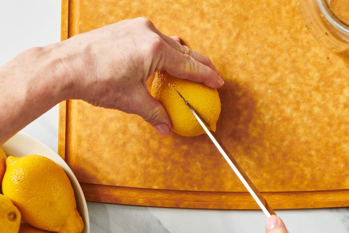 Slicing fresh lemon into quarters on wood cutting board with knife.