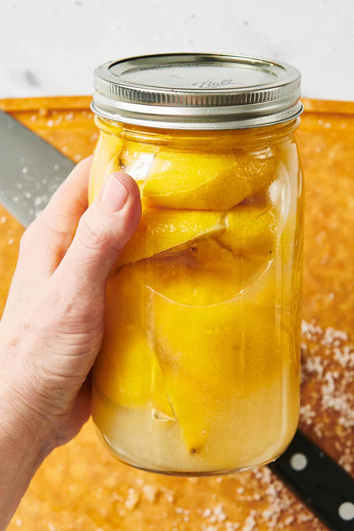 Woman holding jar of preserved lemons over wood cutting board.