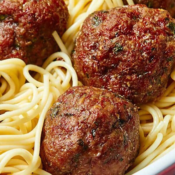 Giant meatballs in serving bowl on spaghetti.