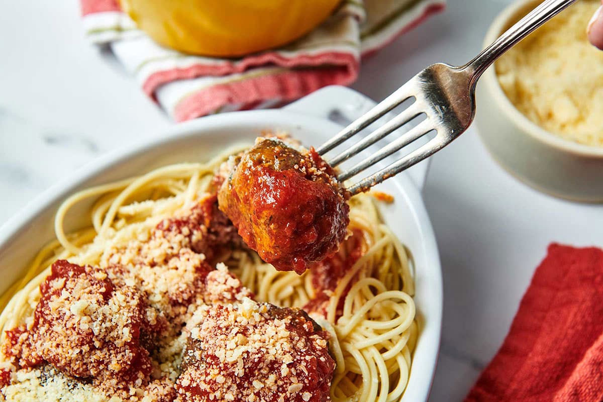 Fork grabbing a meatball from a bed of pasta with marinara sauce.