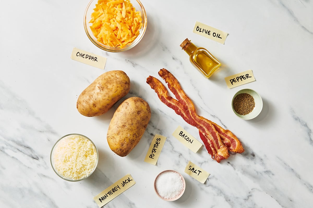 Potatoes, bacon, cheese, and other loaded potato skins ingredients on table.