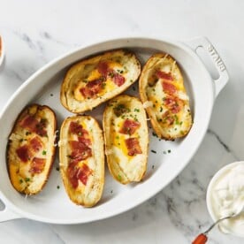 Loaded potato skins in white serving dish with condiments.