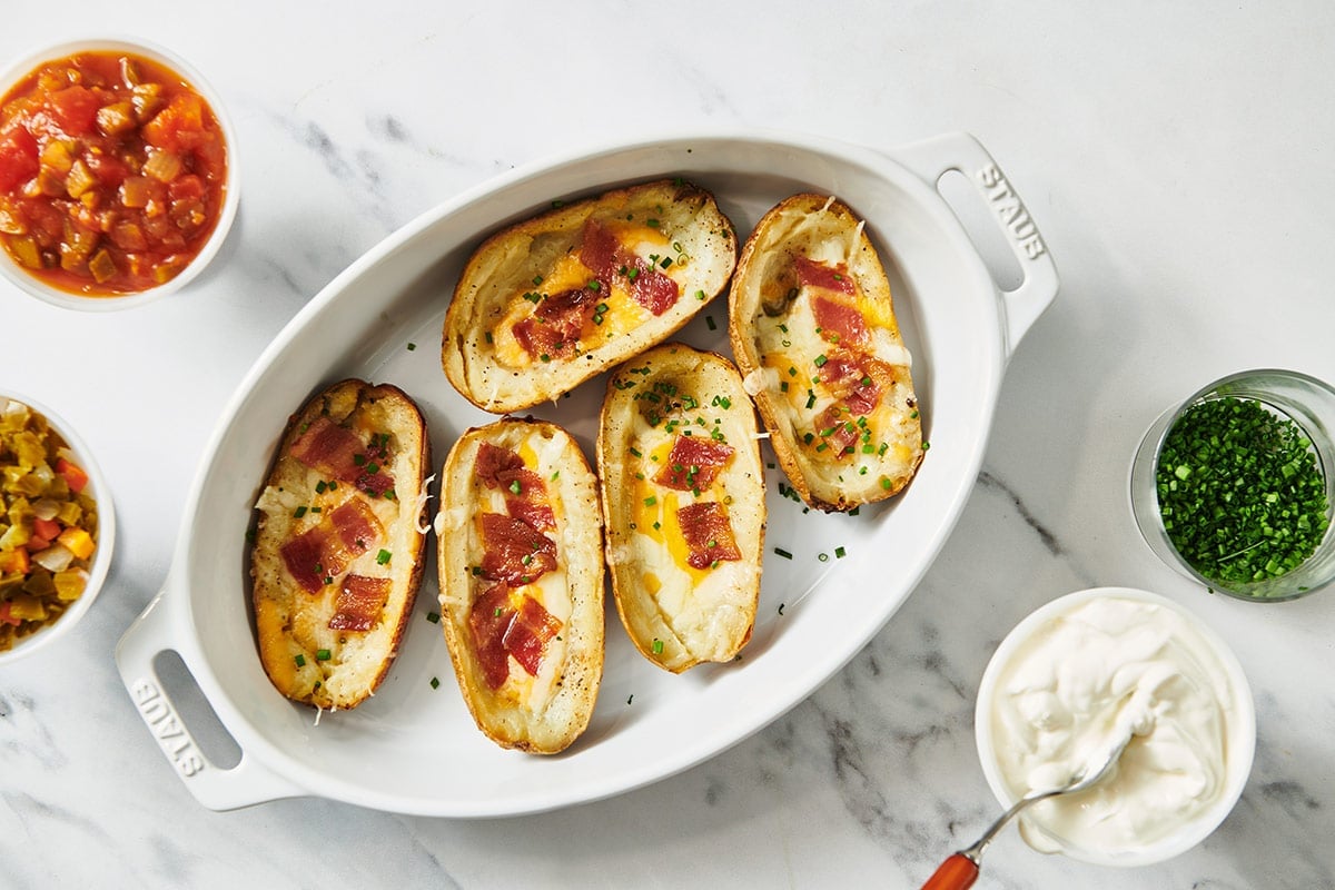 Loaded potato skins in white serving dish with condiments.