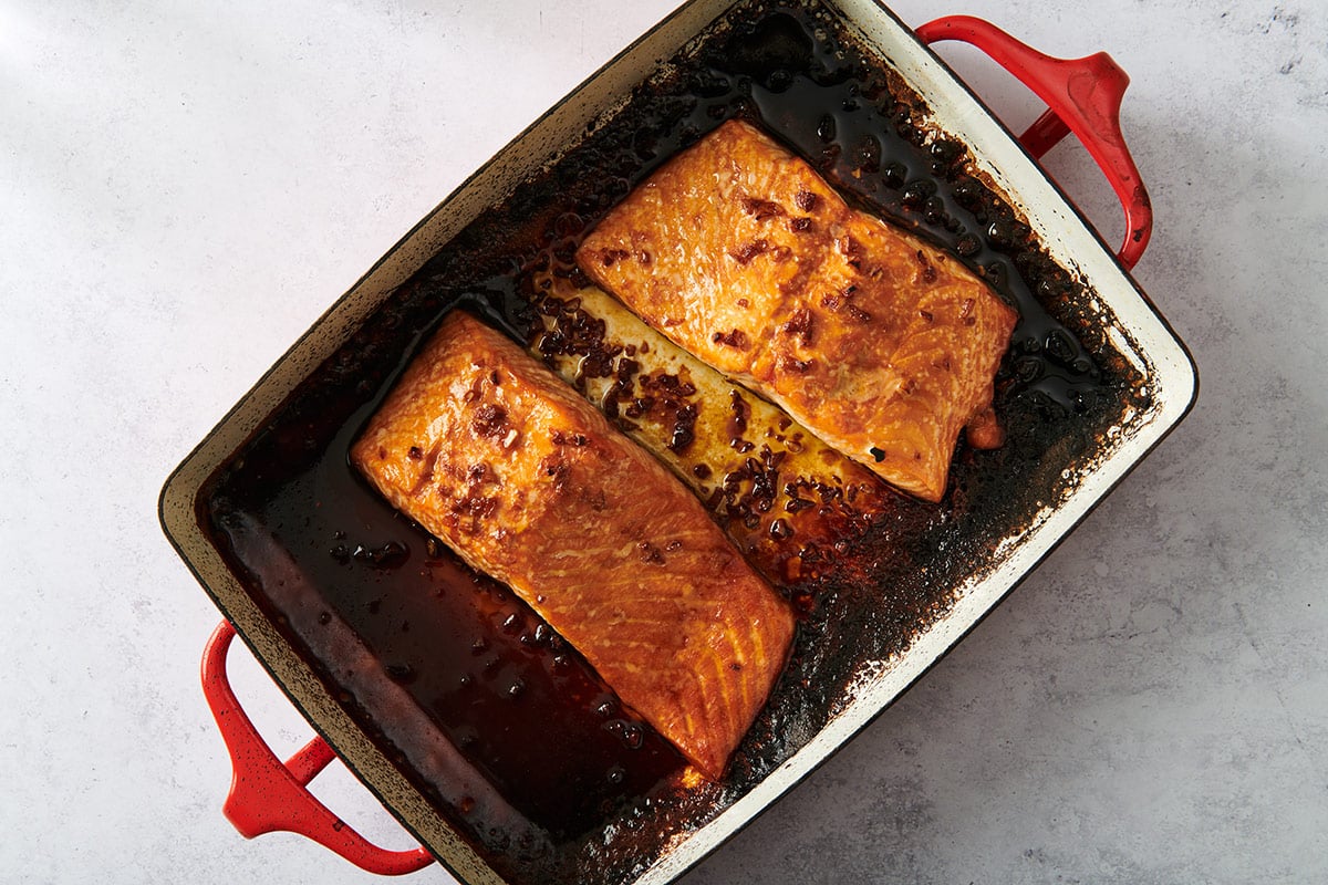 Broiled salmon filets with teriyaki sauce in red baking pan.
