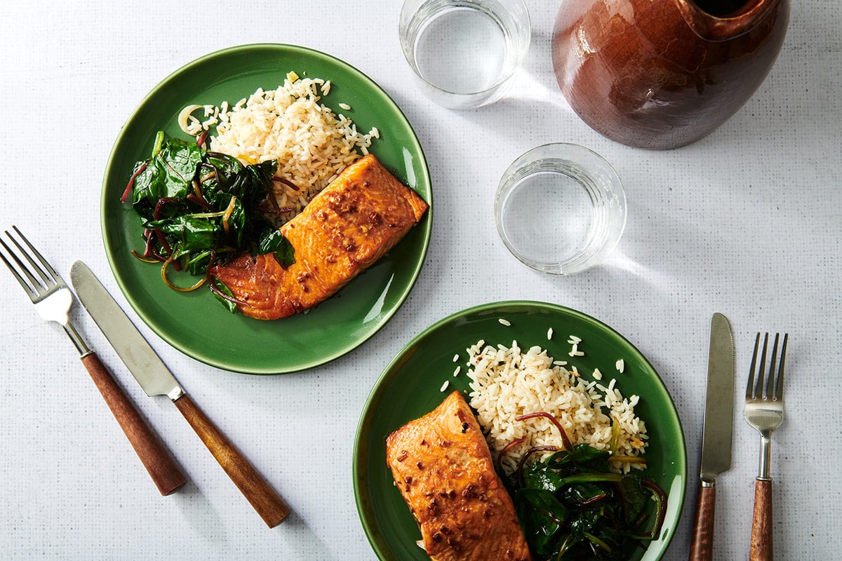 Two green plates on table with teriyaki salmon, greens, and rice.