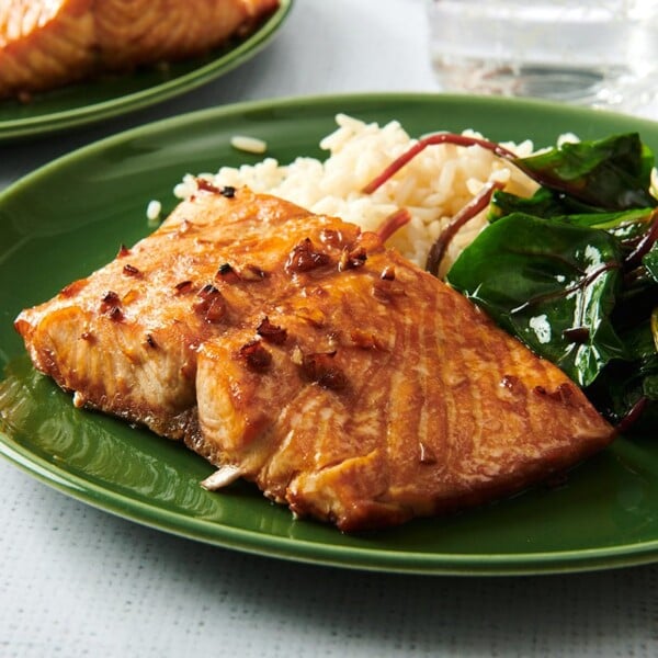 Teriyaki salmon on green plate with a side of sauteed greens and rice.