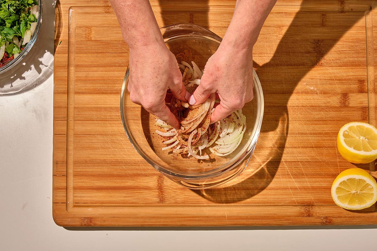 Massaging finely sliced onions for Turkish Chickpea Salad in glass bowl.