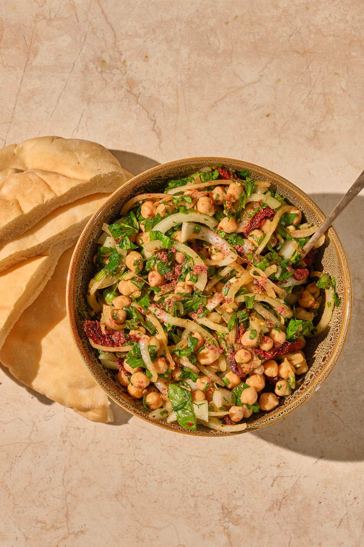 Turkish Chickpea Salad in brown bowl with serving spoon and side of pita bread.