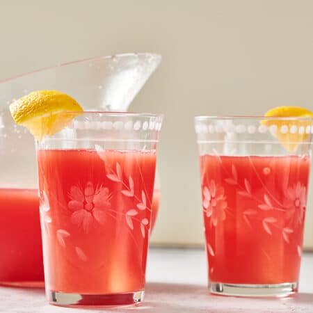 Homemade watermelon lemonade in pitcher and glasses garnished with lemon wedges.