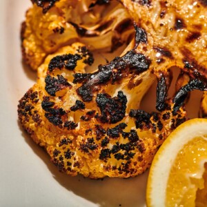 Grilled cauliflower on plate with lemon wedge.