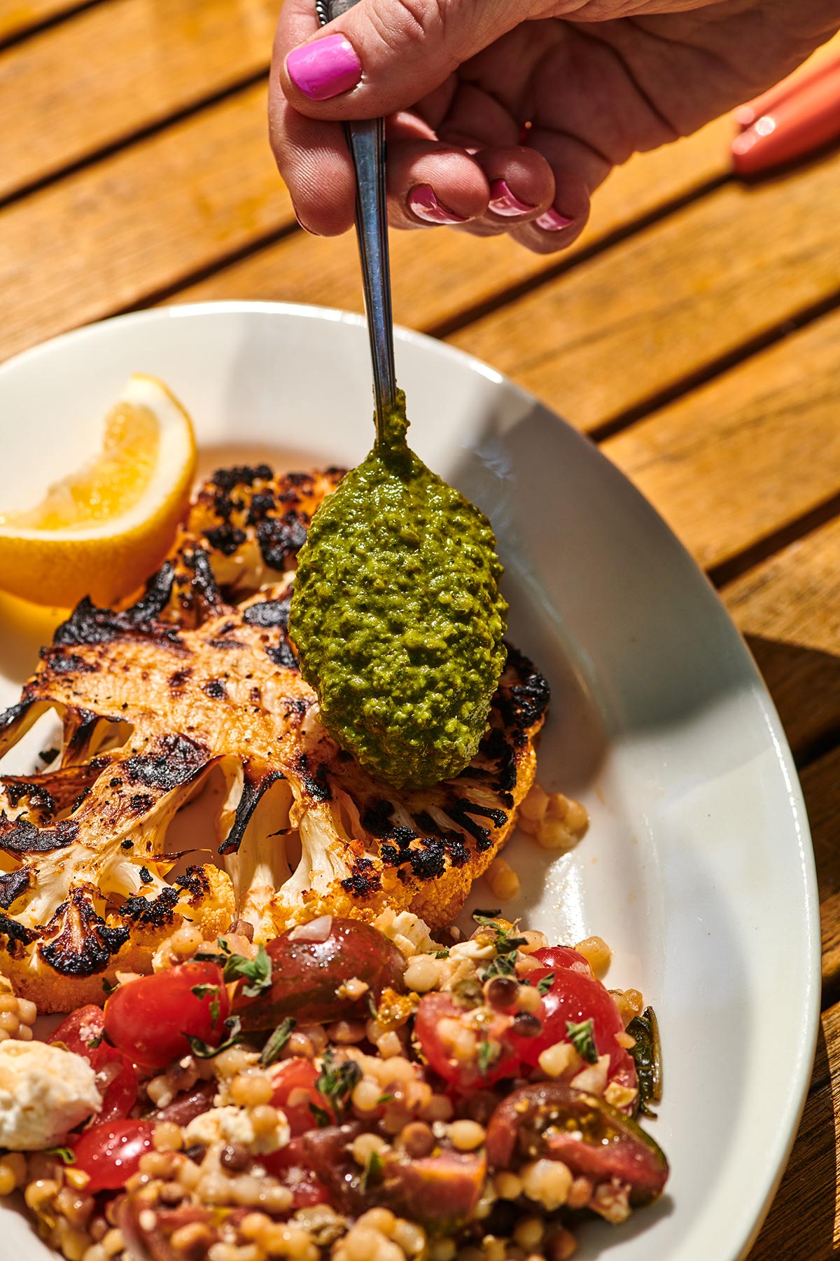 Drizzling chimichurri sauce over a plate of grilled cauliflower.