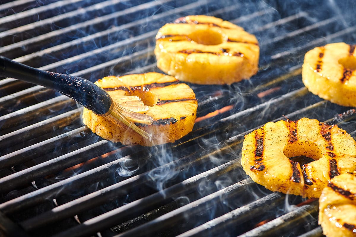Applying brown sugar glaze to pineapple on the grill with a brush.