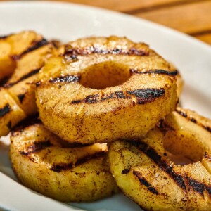 Grilled pineapple slices on white plate at picnic.